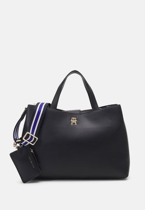 Sac à main en cuir noir avec doubles anses, logo doré, bandoulière réglable rayée bleu et blanc, et pochette zippée noire attachée.