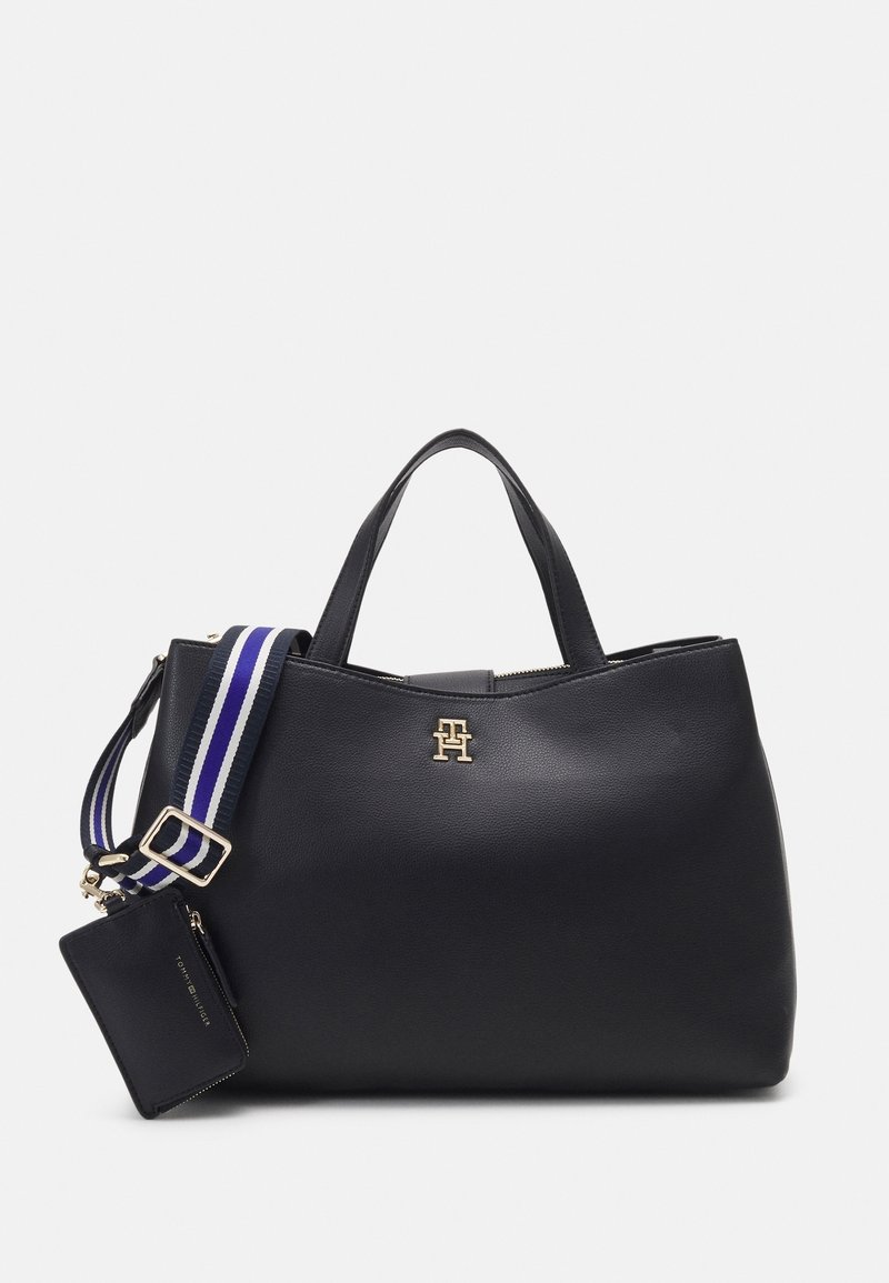 Sac à main en cuir noir avec doubles anses, logo doré, bandoulière réglable rayée bleu et blanc, et pochette zippée noire attachée.