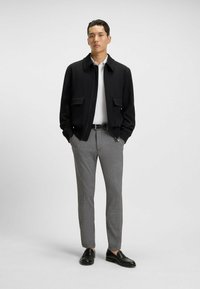 Czarna kurtka na zamek z dwoma przednimi kieszeniami, biała koszulka polo, szare spodnie w kratkę i czarne loafersy. Gładkie materiały i dopasowany krój.