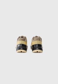 Pair of beige and black athletic shoes viewed from the back on a plain white background.