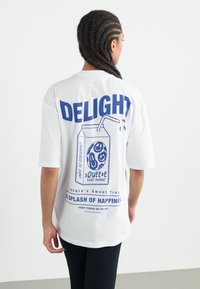 Hvid bomulds T-shirt med et blåt grafisk design af et juicekarton og legende tekst. Løs pasform med korte ærmer og rund halsudskæring.