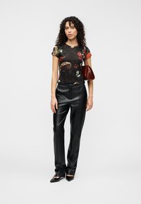 Μαύρο στενό t-shirt με λουλουδάτο μοτίβο συνδυασμένο με ψηλόμεσο μαύρο παντελόνι από ψεύτικο δέρμα. Το μοντέλο κρατά μια μικρή μπορντό τσάντα χειρός με γυαλιστερό φινίρισμα.