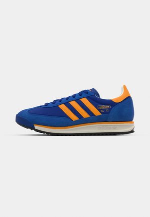 Blaue Wildlederschuhe mit orangefarbenen Streifen, ausgestattet mit einem niedrigen Profil, einer strukturierten Gummisohle und kontrastierenden Akzenten an der Ferse und der Zunge.