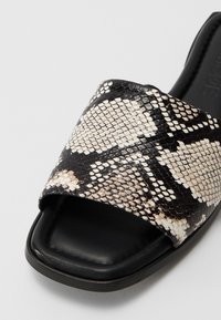 Schwarze und beige Schlappen mit strukturiertem Schlangenprint-Obermaterial, offenes Zehendesign und schwarze Gummisohle. Glatte Lederdetails.