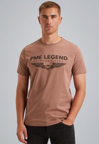 Hnědé bavlněné tričko s černým grafickým potiskem "PME LEGEND AMERICAN CLASSIC" a křídly, krátkými rukávy a kulatým výstřihem.
