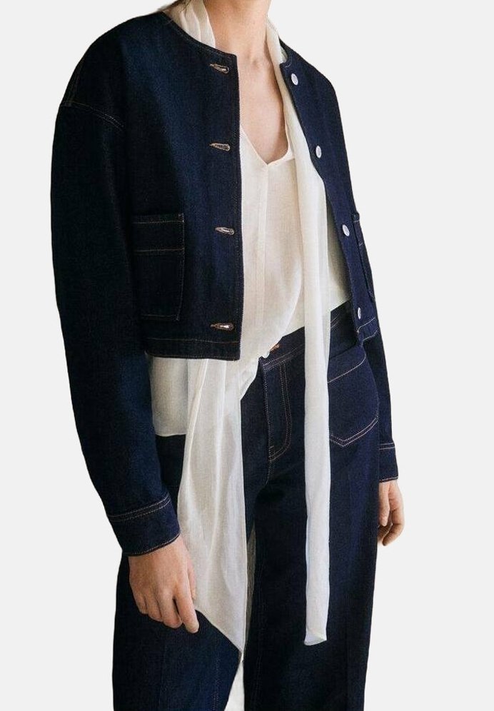 Personne portant une veste courte bleu foncé et un pantalon assorti avec un chemisier blanc avec de longs liens lâches à l'avant.