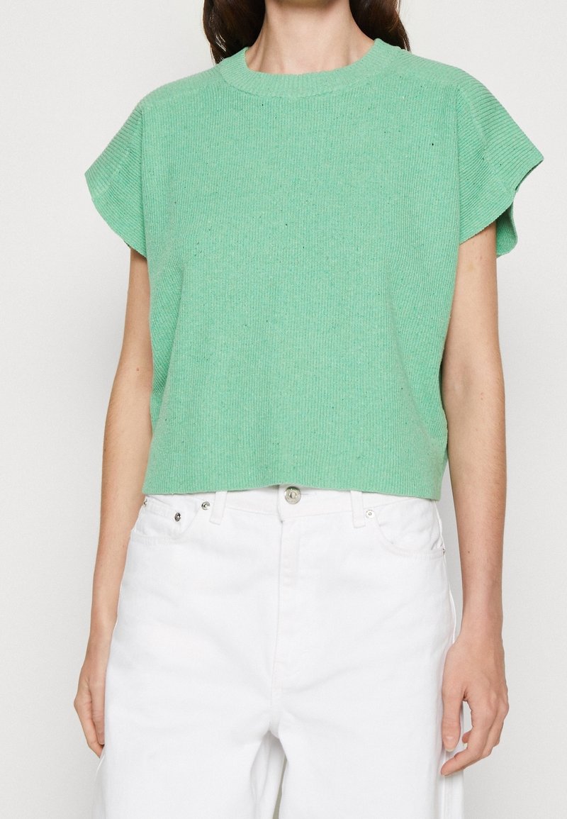 Zielony prążkowany krótki rękawowy sweter z okrągłym dekoltem oraz lekko rozszerzanymi rękawami, zestawiony z białymi spodniami o wysokim stanie.