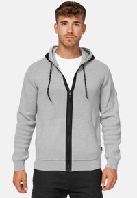 Hoodie zippé gris avec une doublure de capuche noire, des poches avant et une fermeture éclair noire contrastante. Dispose de cordons réglables et de poignets côtelés.