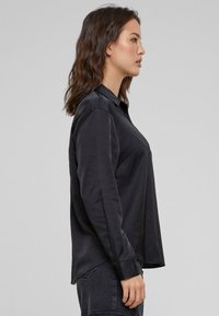 Zwarte langermige shirt met een kraag, gladde textuur, zijnaad details en een relaxte pasvorm, gecombineerd met donkere spijkerbroek.
