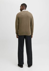 Olive roheline villane sviiter, millel on lõdva istuvuse, ümmargune kaelus ja soonikkoes mansetid, kombineeritud mustade laiadest pükstest. Lihtne disain, minimaalne detailide arv.