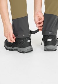 Musta ulkoilukengät harmailla yksityiskohdilla, joita on käytetty kapenevien housujen kanssa, joissa on tummanharmaa lahje, kiinnitetty neppareilla ja hihnalla.