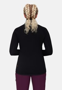 Maglietta nera a manica lunga con un design aderente e una texture liscia. Presenta maniche raglan e un accento arancione vicino all'orlo, abbinata a pantaloni viola.