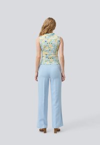Sleeveless, floral print top in pastel colors; paired with light blue wide-leg trousers. Smooth fabric, fitted bodice, minimalistic design.