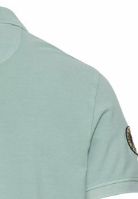 Lichtgroene polo met een textuurstof, een klassieke kraag en een ronde logopatch op de linkermouw. Korte mouwen.