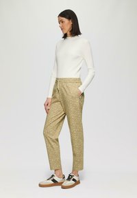Lichtgewicht, geribbelde witte lange mouw top gecombineerd met gebloemde, beige broek met elastische taille. Schoenen hebben een mix van beige, zwart en wit.