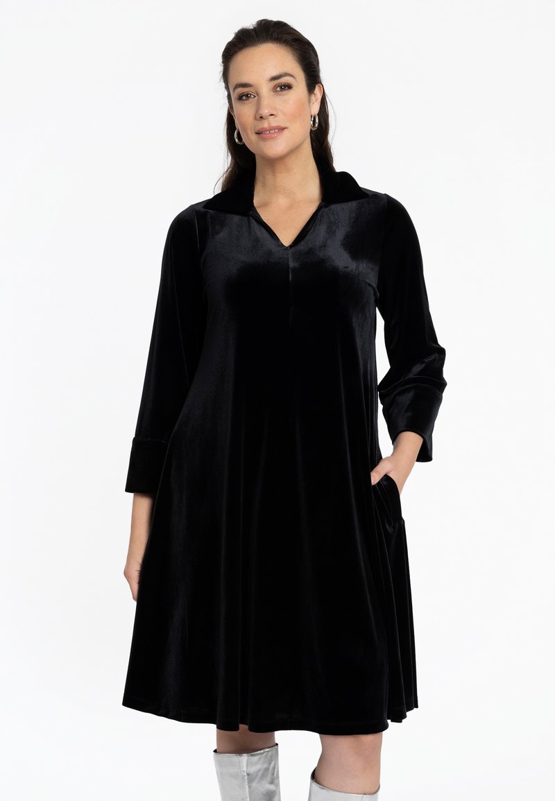 Robe en velours noir avec un décolleté en V et un col, des manches à trois quarts et des poches latérales. Texture lisse avec une forme évasée.