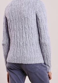 Vaaleanharmaa neulepoolo, jossa on teksturoitu kuvio. Varressa ja helmassa ribbaus, sekä rento istuvuus ja hieman kaareva takaosa.