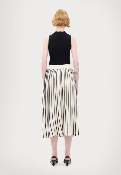 Schwarzes geripptes ärmelloses Top, kombiniert mit einem knöchellangen, cremefarbenen Rock mit vertikalen schwarzen Streifen. Das Model trägt schwarze Absatzsandalen.