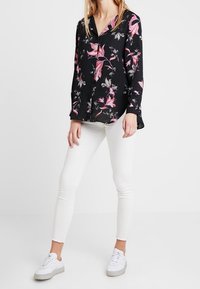 Czarna bluzka z różowo-białym nadrukiem kwiatowym, długie rękawy, zapinana na guziki, zestawiona z białymi dopasowanymi dżinsami i białymi sneakersami.