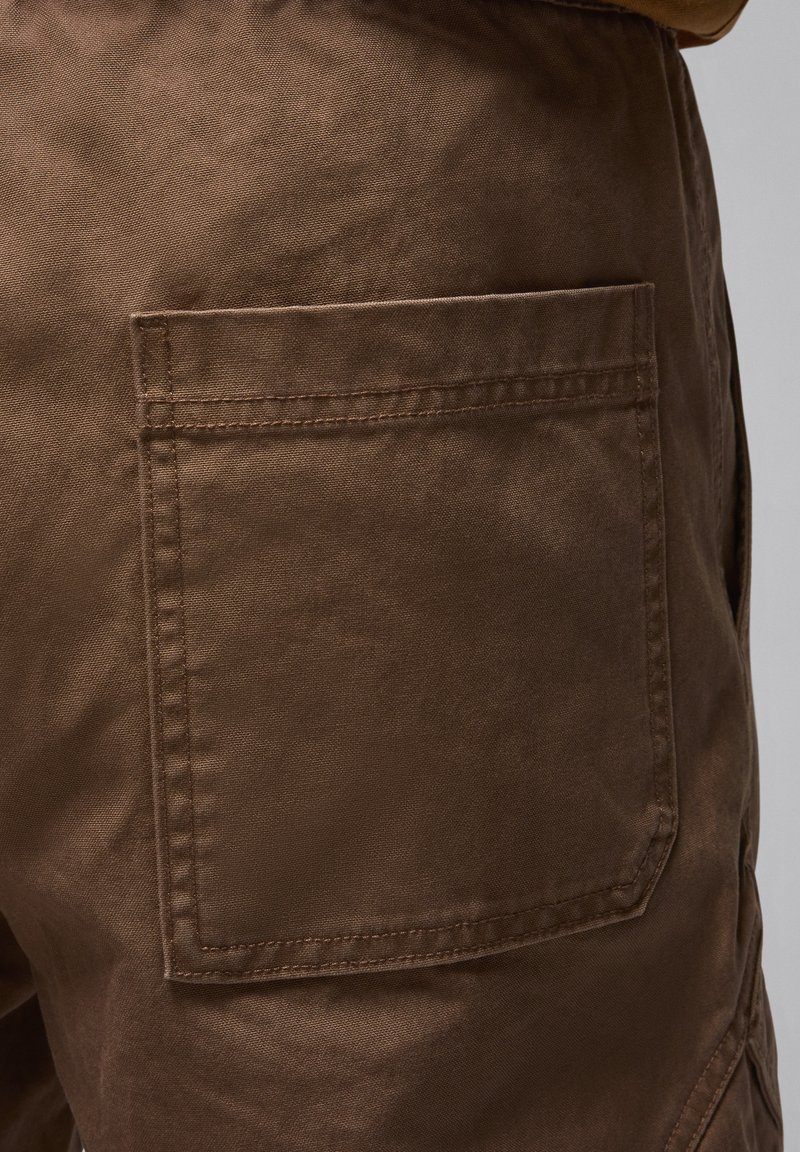 Shorts in cotone marrone con tasca posteriore piatta con bordi cuciti, texture liscia e design casual.