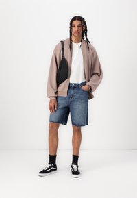 Overdimensioneret beige bomberjakke, hvid henley skjorte, blå denim shorts, sort crossbody taske, sorte strømper og sorte sneakers.