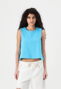 Light blue, sleeveless cropped top with a round neckline, made of soft fabric. Paired with white distressed shorts, showcasing a relaxed fit.