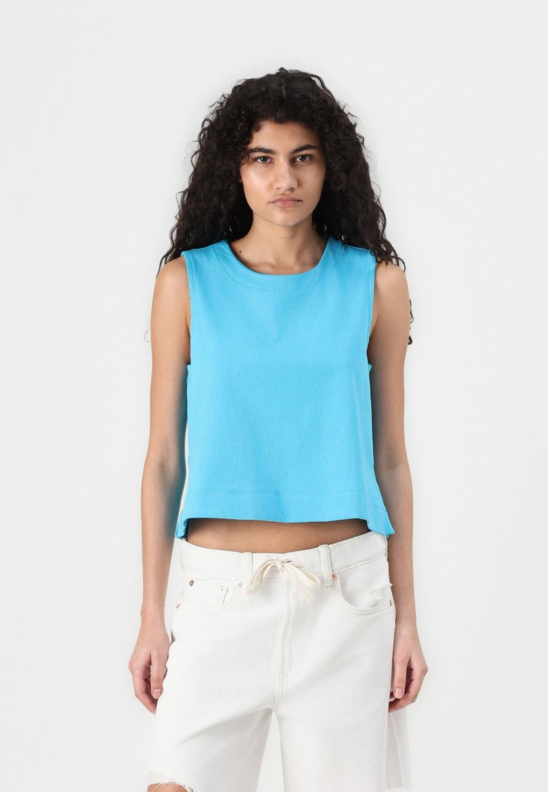 Light blue, sleeveless cropped top with a round neckline, made of soft fabric. Paired with white distressed shorts, showcasing a relaxed fit.