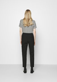 Zwarte broek met een slim fit, voorzien van een achterzak. Gepaard met een grijs T-shirt met korte mouwen. Het materiaal lijkt soepel, met een casual ontwerp.