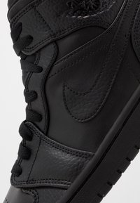 Gros plan d'une basket en cuir noir avec des panneaux texturés, des lacets noirs et un logo Nike Swoosh cousu sur le côté.