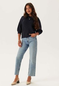 Marinblå stickad tröja med korta, ballongärmar som kombineras med ljusblå raka jeans och nude blockklackar.