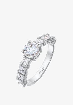 Srebrny pierścionek z okrągłym, centralnym przezroczystym kamieniem oraz mniejszymi przezroczystymi kamieniami osadzonymi wzdłuż obrączki, charakteryzujący się wypolerowaną, gładką powierzchnią i osadzeniami z pazurami.