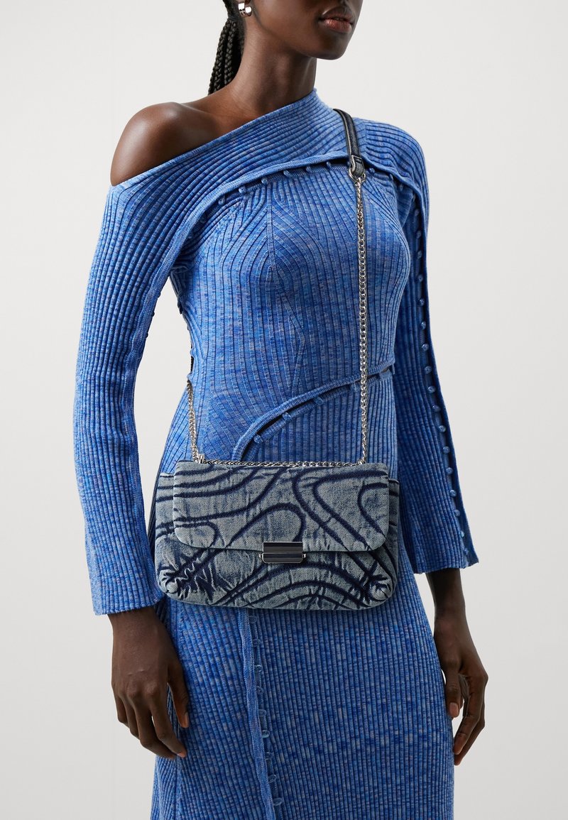 Abito blu a righe con maniche lunghe e design off-shoulder. Borsa trapuntata blu e grigia con tracolla a catena, caratterizzata da un motivo astratto e chiusura nera.