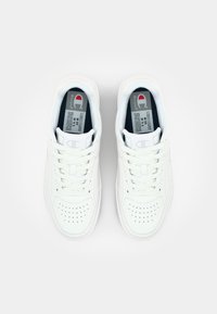 White leather sneakers with perforated toe, flat laces, and a padded collar. Features a logo on the tongue and inside label detailing size.