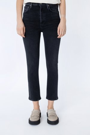 Person iført sorte slim-fit ankel-lange jeans kombineret med beige ruskind loafers mod en hvid baggrund.