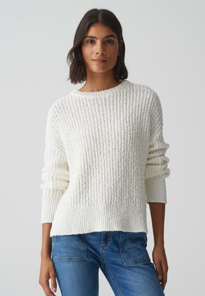 Chunky white knit sweater with a ribbed texture, round neckline, and dropped shoulders, paired with blue denim jeans.