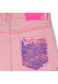 Rózsaszín farmer rövidnadrág fényes, kék és lila árnyalatú flitteres zsebbel, valamint élénk rózsaszín címkével a derékrész közelében.