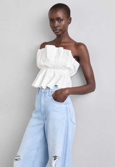 Vit strapless topp med volangstruktur, åtsittande i midjan, kombinerad med ljusblå högmidjade jeans med slitna detaljer.