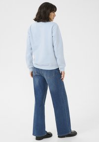 Ljusblå sweatshirt med rund halsringning, ribbade mudd och nederkant. Matchas med vida jeans i denim med bakfickor och en mörk tvätt.