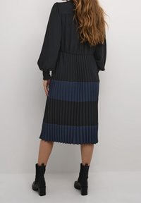 Plea veckad midiklänning i svart och mörkblått. Mjukt tyg med puffärmar, åtsittande midja och kontrasterande horisontella ränder. Svarta ankelboots.