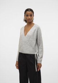 Gray wrap sweater with a deep V-neck and long sleeves, featuring a tie detail on the side. Soft, textured fabric. Paired with black trousers.
