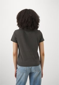 Camiseta de manga corta gris oscuro con un detalle en el cuello en forma de V, combinada con jeans de mezclilla azul claro, vista desde la parte posterior. Textura suave.