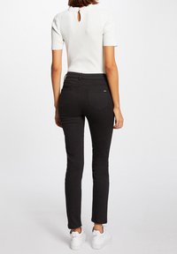 Zwarte slim-fit jeans met een middelhoge taille, functionele achterzakken, gecombineerd met een witte top met een sleutelgatdetail op de rug.