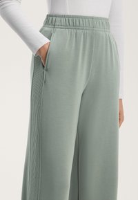 Ljust gröna, vida sweatpants i mjukt tyg, med resår midja, sidofickor och strukturerade vertikala detaljer.