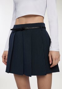 Gonna plissettata blu navy con righe bianche, dotata di una cintura nera. Realizzata in tessuto, che esalta la forma con una struttura definita e una texture liscia.