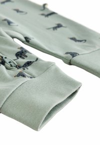 Vêtements à manches longues en tissu vert avec des motifs d'animaux ludiques. Les poignets sont côtelés pour un ajustement confortable. Le matériau semble doux et texturé.