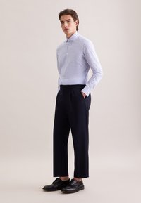 Camicia a righe blu e bianche con colletto a punta, abbinata a pantaloni plissettati blu scuro e scarpe nere stringate.