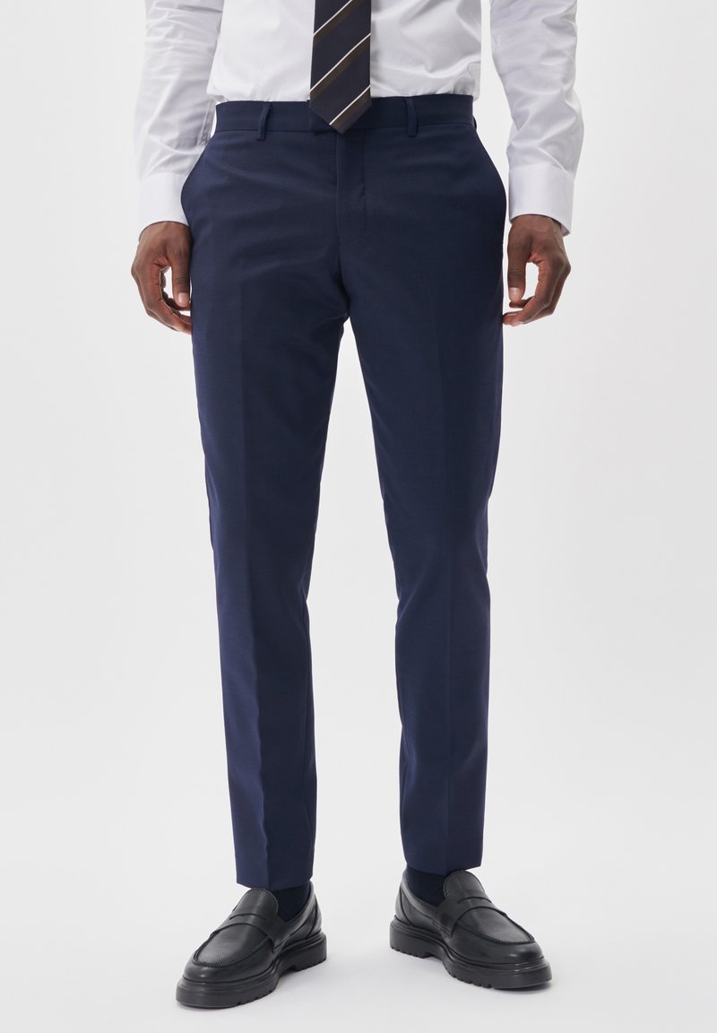 Mörkblå skräddarsydda byxor i mjukt tyg; har raka ben, bälteshällor och framfickor. Kombinerade med svarta loafers.