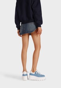 Scarpe da ginnastica blu con dettagli e lacci bianchi, abbinate a un maglione scuro e a una mini gonna di denim con orlo curvo.