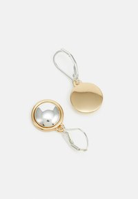Boucles d'oreilles en métal doré et argenté en forme de créole avec des centres argentés arrondis et réfléchissants, et des arrières plats dorés, dotées d'une fermeture à levier.