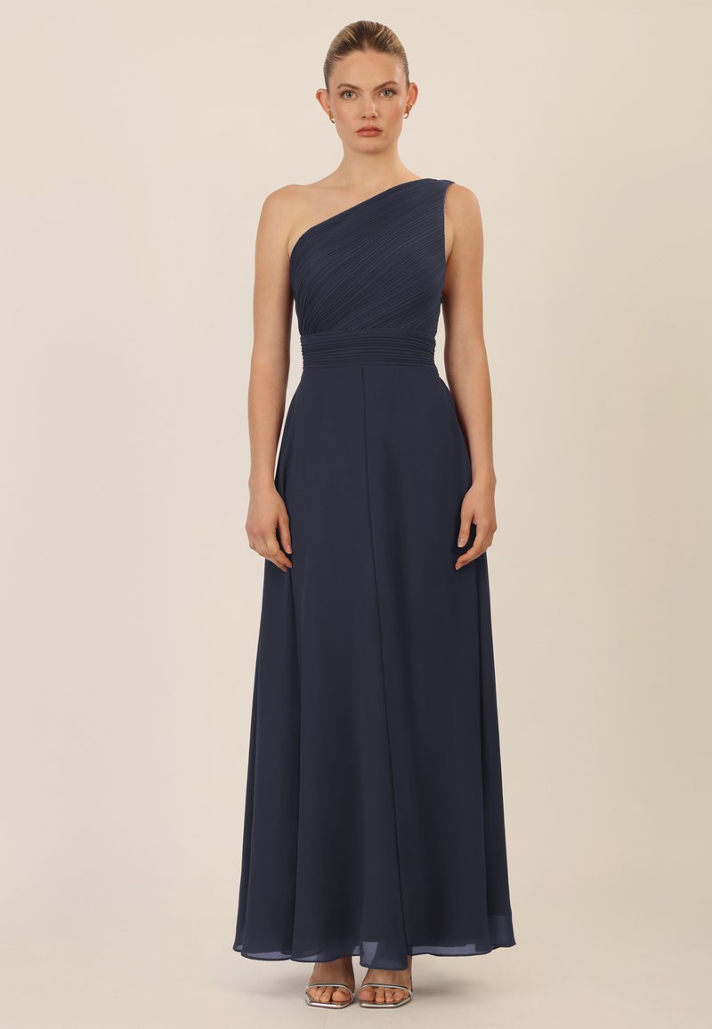Ein ärmelloses dunkelblaues Kleid aus fließendem Stoff, mit einem gefalteten Oberteil, flachem Taillenbund und einem knöchellangen Rock mit einem leichten Glanz.